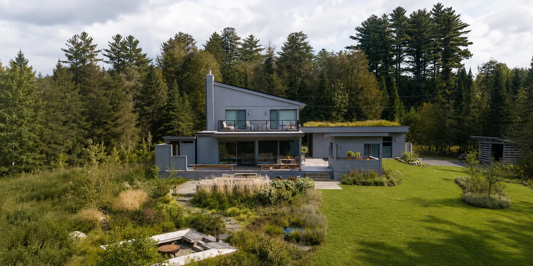 Modern Vermont home with grey siding, a green roof, and a native meadow garden at the forest edge
