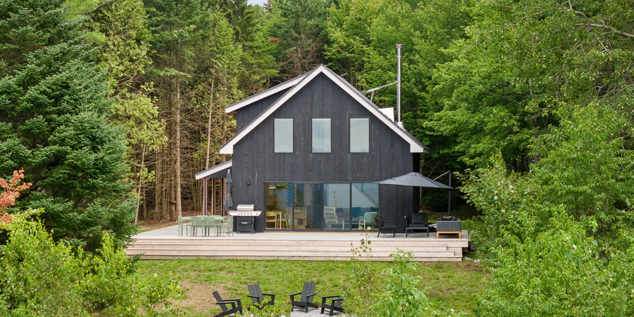 Beach Hill Camp in Glover, Vermont: a charred-board cabin with a wide deck and fire pit at the edge of the woods